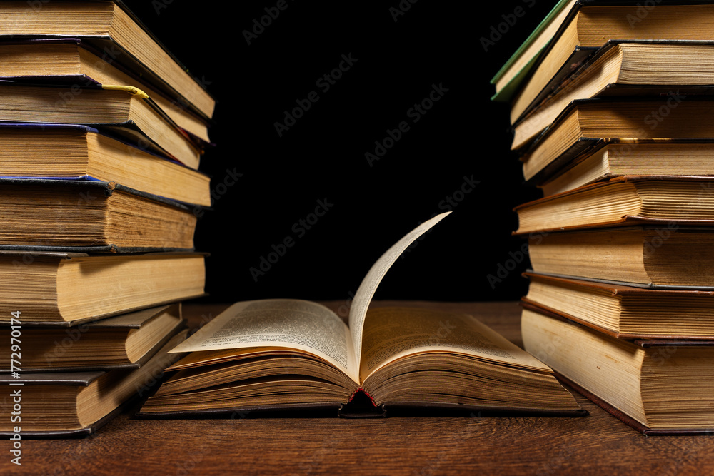 Fototapeta premium Opened book and stacks of old books on wooden desk in old library. Ancient books historical background.