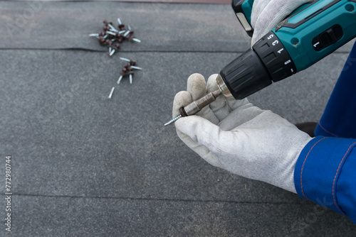 on a dark background of roofing material, a master in white gloves installs a screwdriver into a power tool