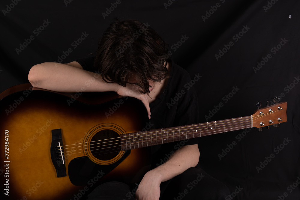 Obraz premium Male teenager with acoustic guitar on black background. With long hair in black clothes