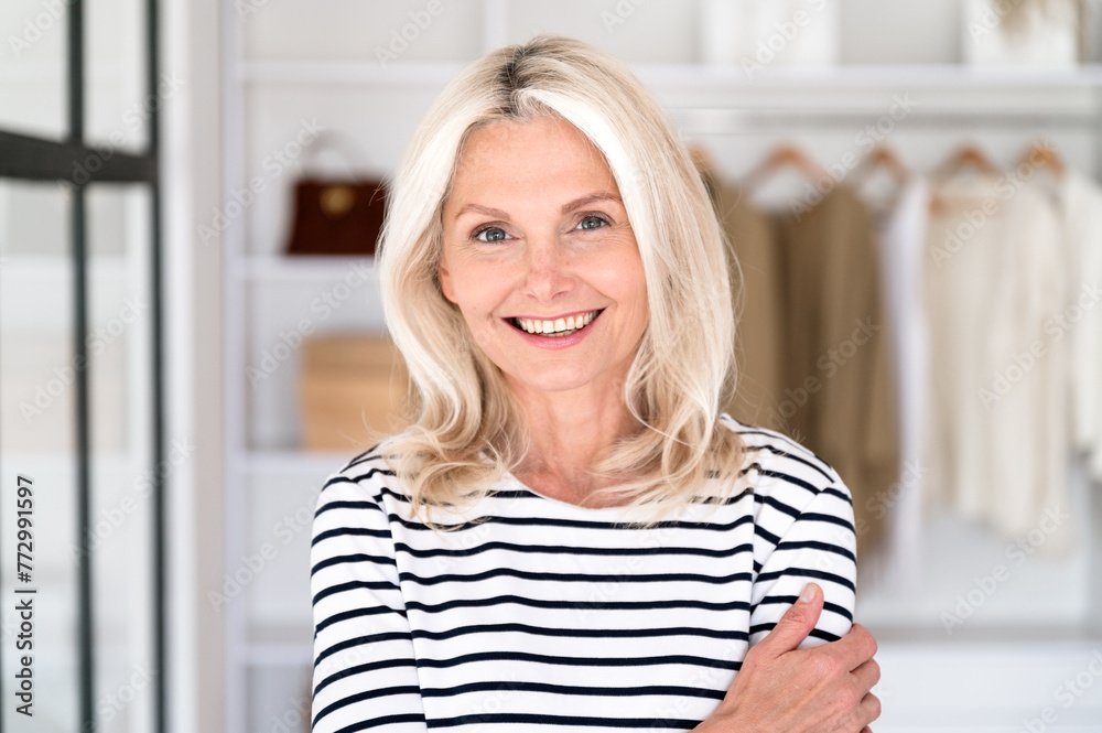 Middle age woman fashion designer standing against new clothes collection in wardrobe
