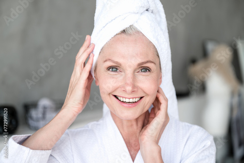 Middle age woman with towel on head look at camera, touch her perfect face