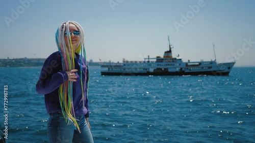 Young hipster girl with colorful dreadlocks walking along embankment against Bosphorus, Turkey. Woman tourist taking steps on seafront, ship sailing at background, Istanbul Galataport photo