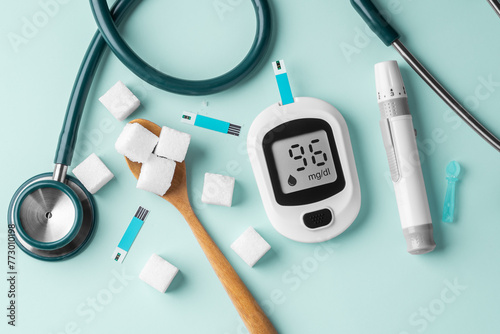Diabetes concept with blood glucose sugar meter, sugar cubes in spoon and stethoscope on green background