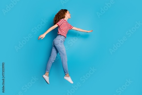 Fototapeta Naklejka Na Ścianę i Meble -  Full length side profile photo of optimistic woman dressed striped t-shirt fly look at offer empty space isolated on blue color background