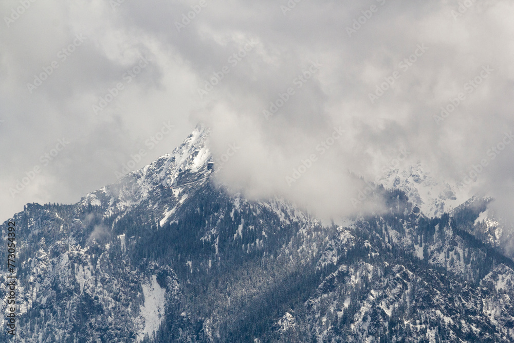 dramatische Unwetterstimmung im Ostallgäu. Wolken hängen vor den schneebedeckten Berggipfeln.