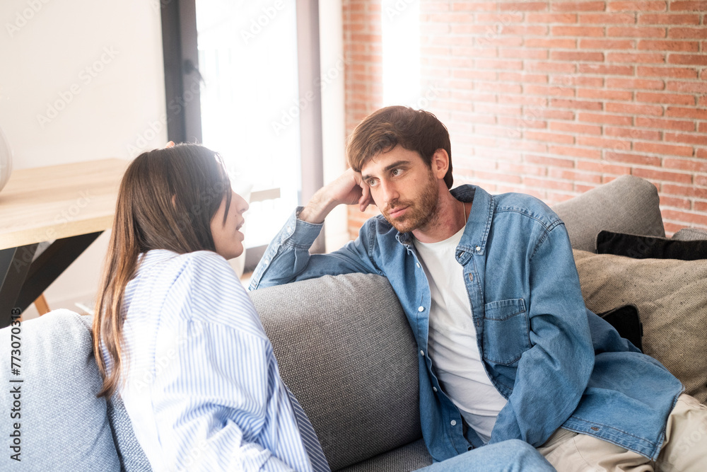 A young 25-year-old couple sits on their cozy sofa in a living room, engaged in a quiet conversation and sharing carefree moments together. Leisure and relaxation concept. Discussion man and woman A young 25-year-old couple sits on their cozy sofa in a living room, engaged in a quiet conversation and sharing carefree moments together. Leisure and relaxation concept. Discussion man and woman