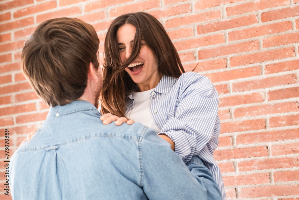 Joyful young couple at home celebrating together having fun and laughing a lot. Man embrace woman with love and friendship. Concept of achievement and success. Relationship and dating people indoor Joyful young couple at home celebrating together having fun and laughing a lot. Man embrace woman with love and friendship. Concept of achievement and success. Relationship and dating people indoor