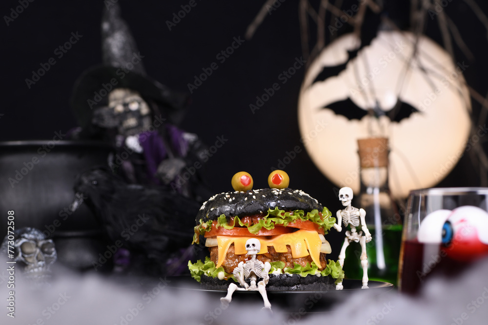Monster Burger. Black bun, juicy beef cutlet, lettuce, onion, tomato and cheese in the shape of teeth, in the company of skeletons. Definitely a pick-me-up and a perfect Halloween party appetizer - obrazy, fototapety, plakaty 