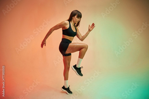 Standing on the one leg, side view. Young woman in fitness clothes is in the studio