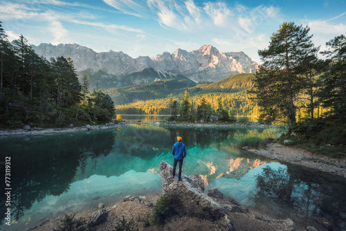 Man enjoying the amazing morning scenery at a gorgeous lake in the Bavarian Alps, with teal water reflecting the view of the mountain range and the nice clouds