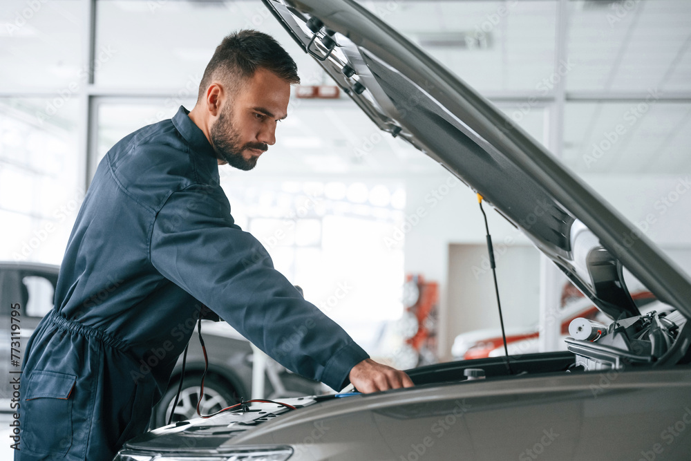 Hood of vehicle is opened. Car repairman is in the garage with automobile Hood of vehicle is opened. Car repairman is in the garage with automobile