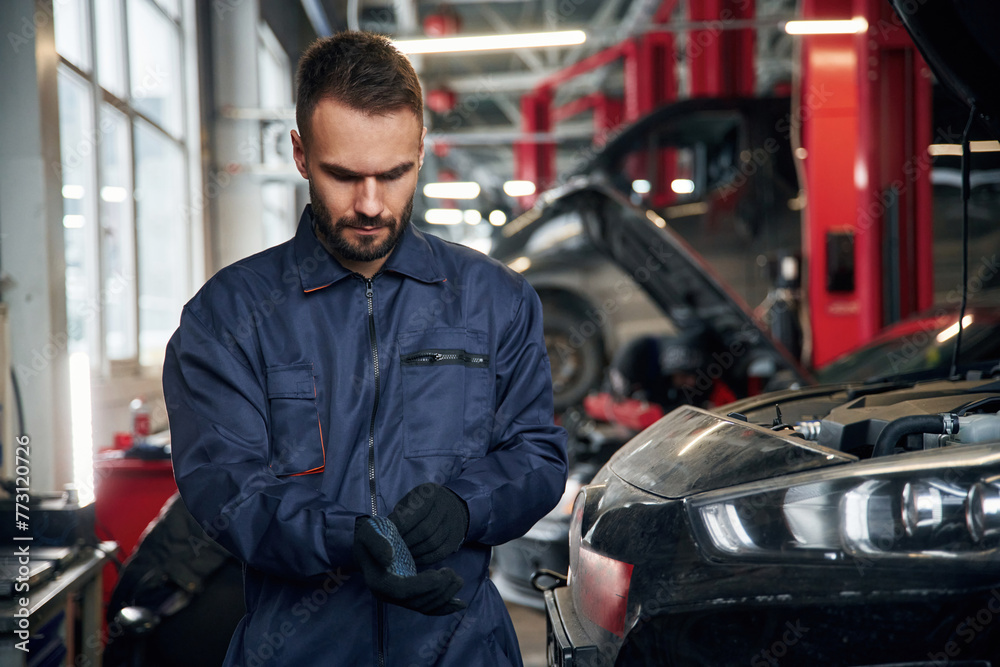Wearing the gloves, standing. Car repairman is in the garage with automobile Wearing the gloves, standing. Car repairman is in the garage with automobile