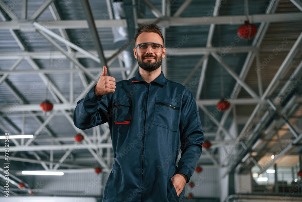 Standing and posing. Car repairman is in the garage with automobile Standing and posing. Car repairman is in the garage with automobile