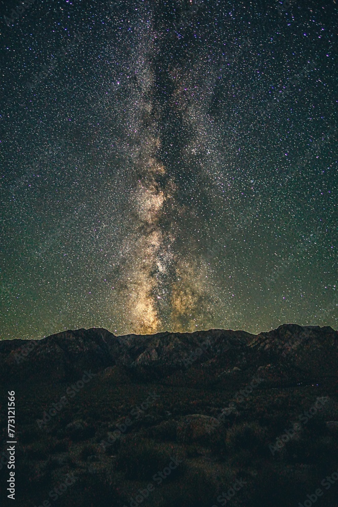 the milky is shining in the dark sky, with mountains behind