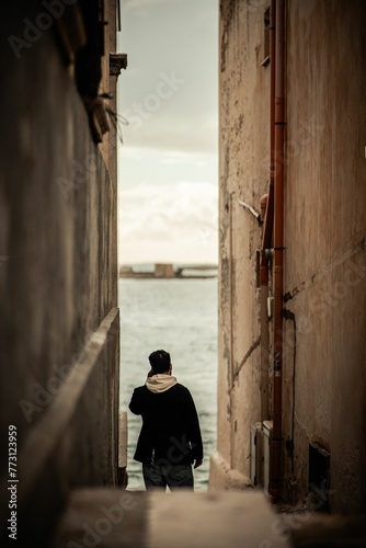 Vertical shot of a person talking on the phone at an alley surrounded by water in Trapani, Italy © Wirestock