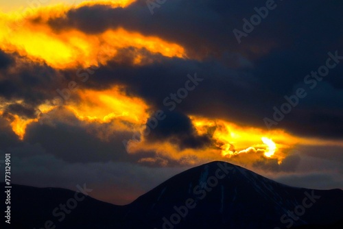 Dramatic orange and yellow sunset sky behind a range of majestic mountain peaks