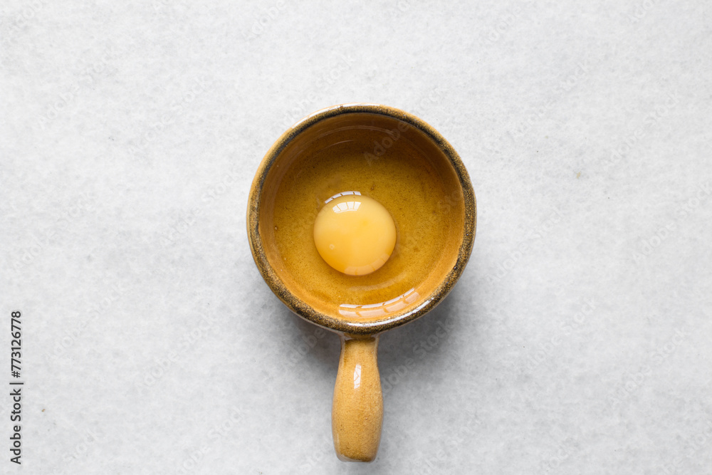 Overhead view of raw egg in a ceramic ramekin, whole raw egg in a ramekin with handle Overhead view of raw egg in a ceramic ramekin, whole raw egg in a ramekin with handle