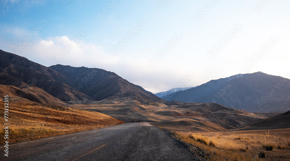 A long winding road through the autumn hills towards the mountains in a blue haze on the horizon.
