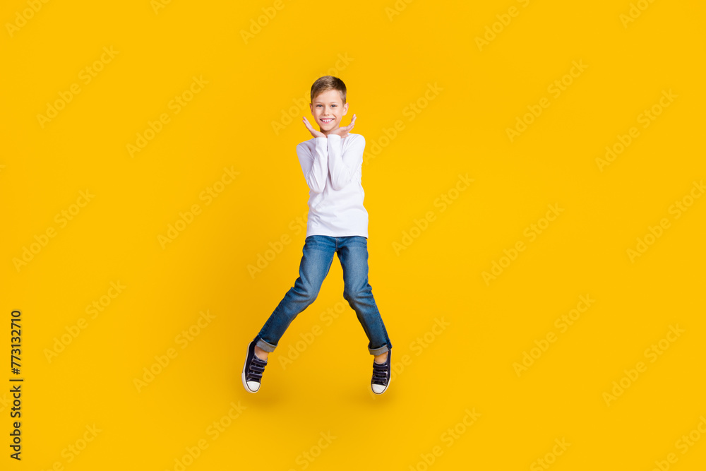 Full length photo of impressed excited boy wear white shirt jumping arms hands cheeks empty space isolated yellow color background