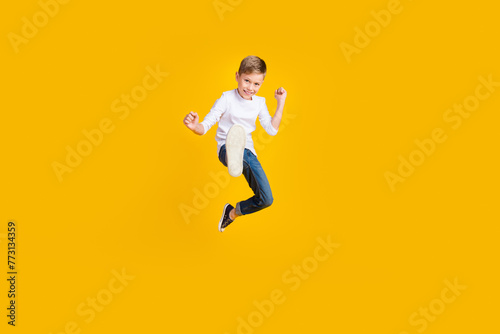Full length photo of positive strong kid dressed white shirt jumping enjoying karate empty space isolated yellow color background © deagreez