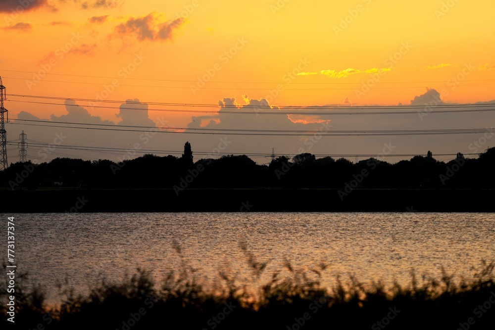 Obraz premium Tranquil lake surrounded by foliage and a majestic sunset sky