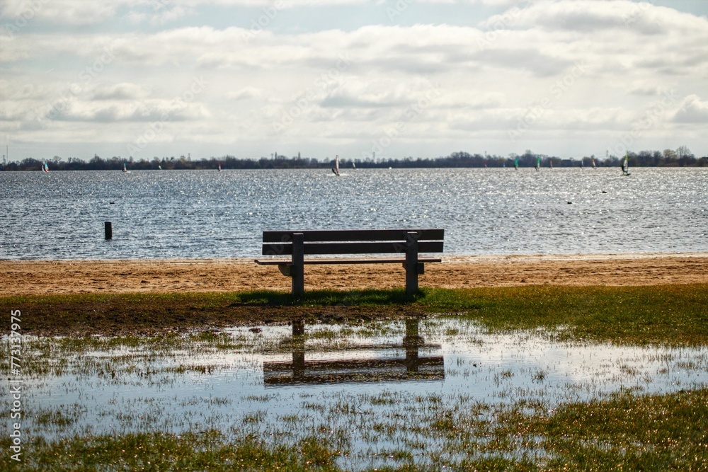 Wooden bench situated on a meadow, with the tranquil calm waters of a lake in the background. Wooden bench situated on a meadow, with the tranquil calm waters of a lake in the background.