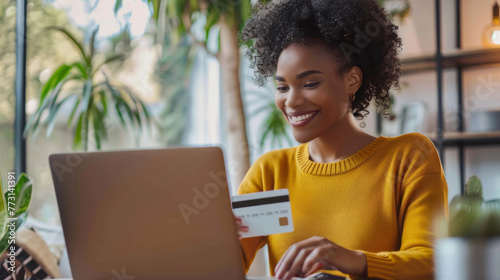 A woman with a credit card in hand smiles while using a laptop.