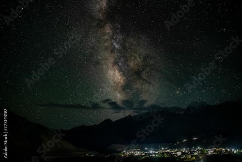 Night sky illuminated by thousands of stars, with silhouettes of mountains visible in the distance.