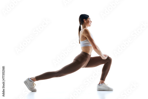 Canvas Print Young woman in white top and leggings stretching legs doing leaps in motion against white studio background