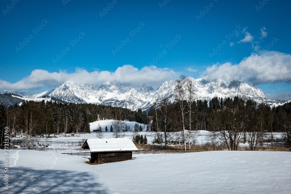 Beautiful mountain landscape with a rustic cabin covered in snow
