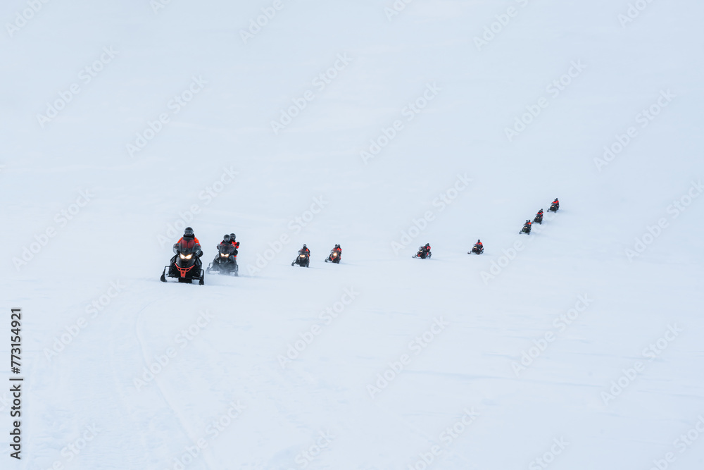 Fototapeta premium Group of tourists riding snowmobiles on snowy glacier mountain