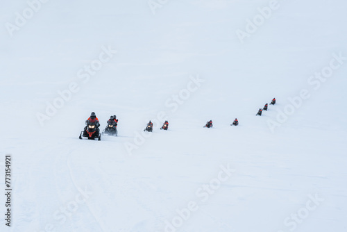 Group of tourists riding snowmobiles on snowy glacier mountain