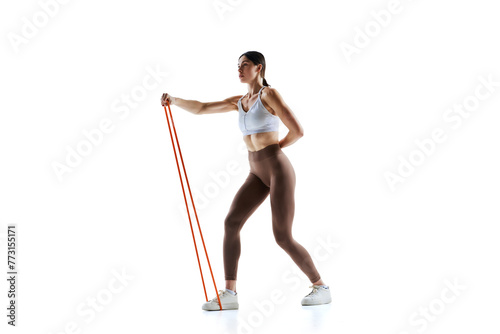 Fit female athlete in fashion top and leggings demonstrating use of exercise band against white studio background. Concept of sport and recreation, movement, self care, action, energy. Ad