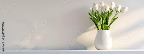 A white vase with white flowers sits on a white shelf
