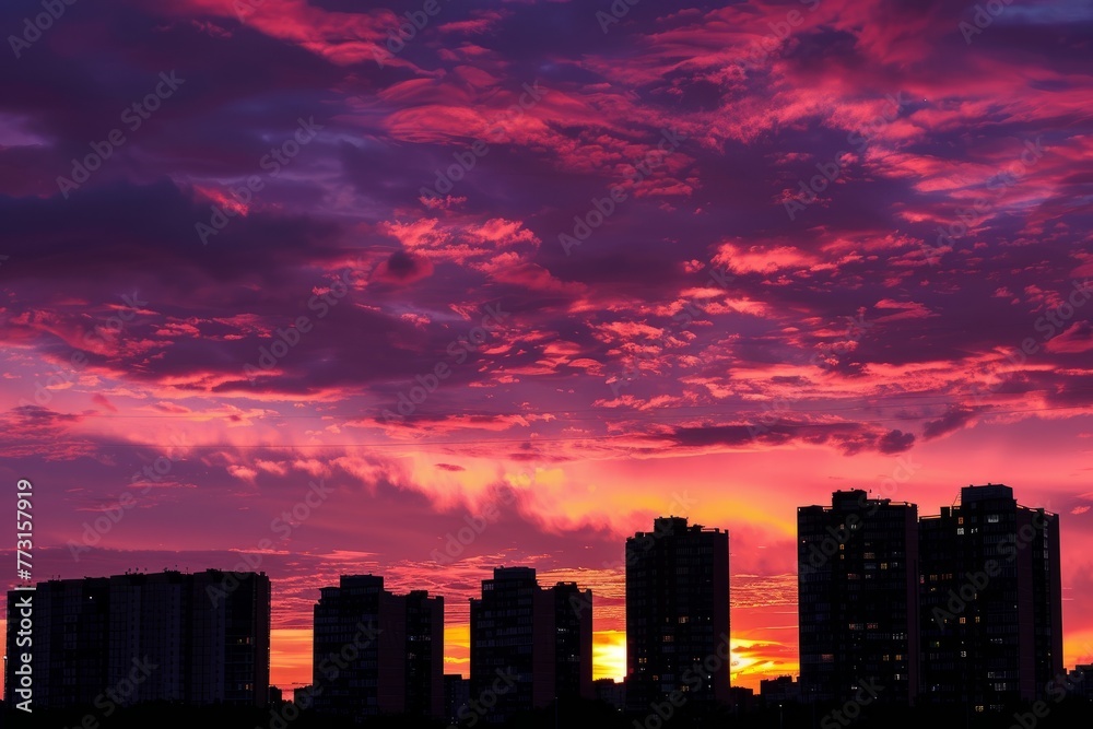 A city skyline stands in silhouette against a vibrant sunset sky, showcasing the buildings in dramatic hues and shadows