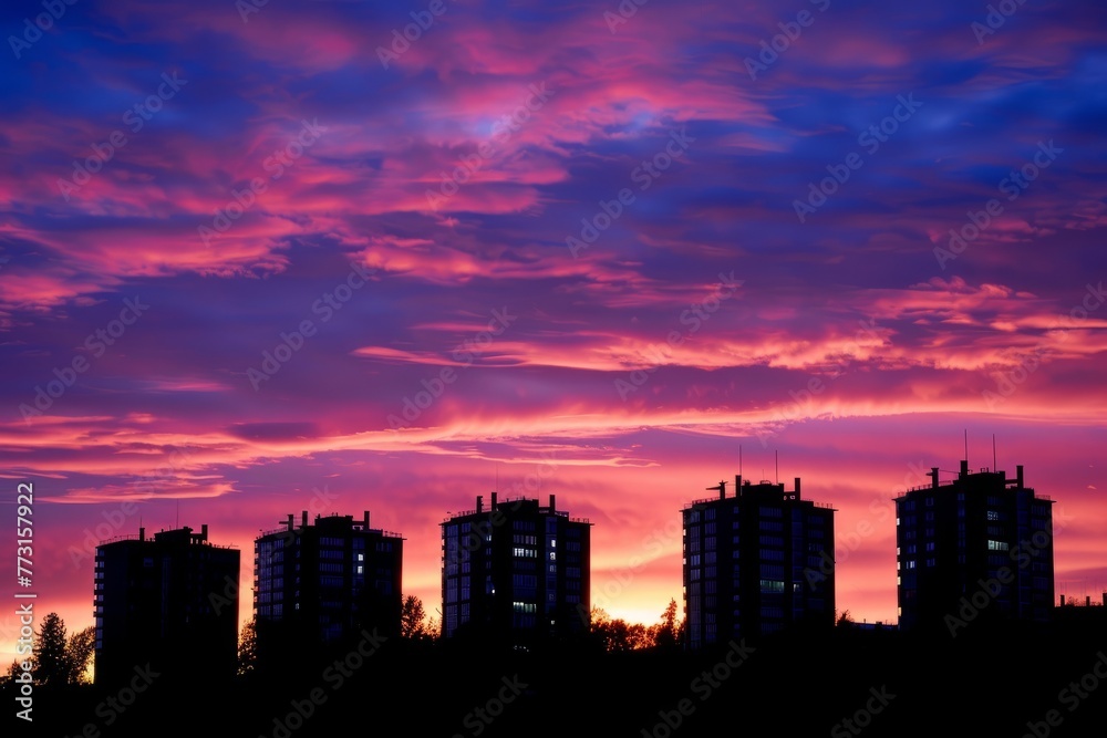 A city skyline at sunset with clouds in the sky, showcasing buildings silhouetted against the vibrant hues of the setting sun