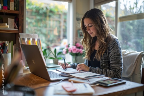 A woman is focused on her work, using a laptop at her home office desk