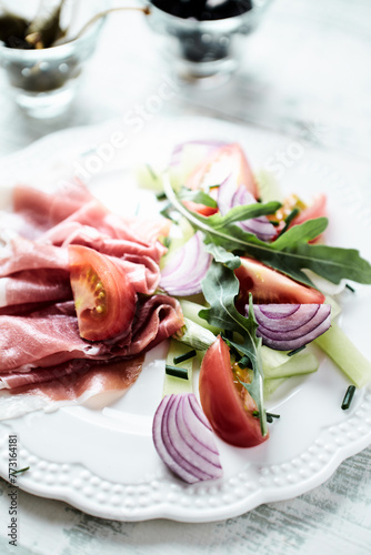 Plate of smoked ham with tomatoes and rocket. Bright wooden background. Close up. 