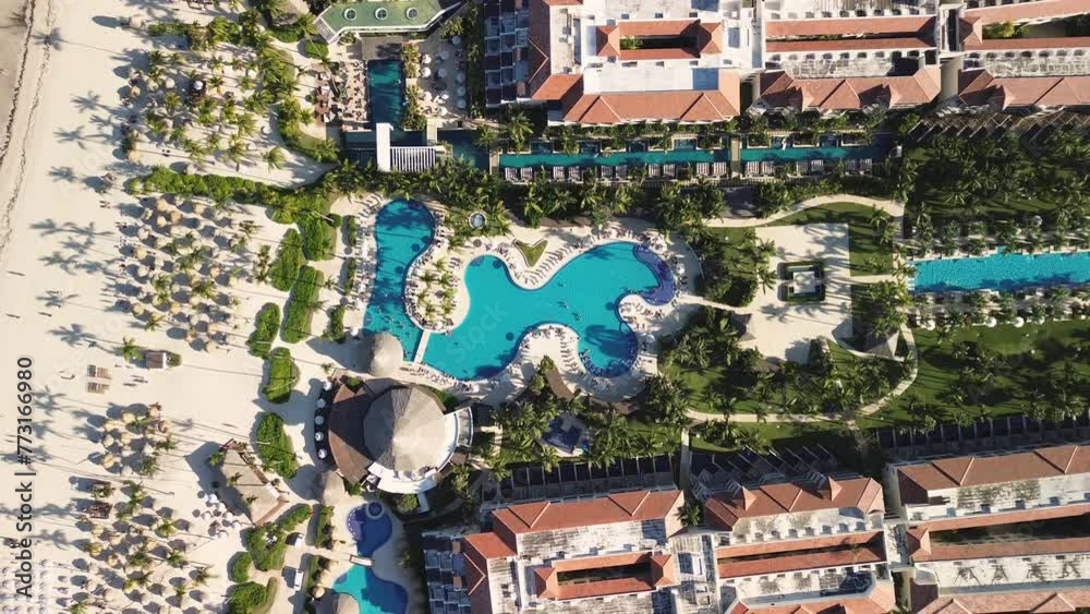 Aerial top view of tropical resort with swimming pool area, family fun in vacation, all inclusive travel and leisure. Oceanfront and beach umbrellas. Sunset. Secrets Royal Beach. Zoom out.