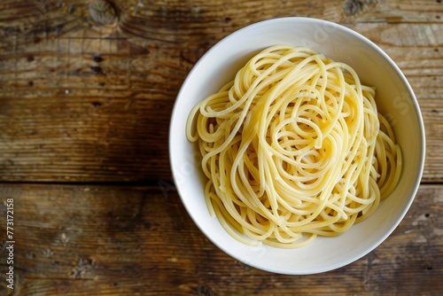 A closeup top-down view of a white bowl filled with artisanal spaghetti on a wooden table