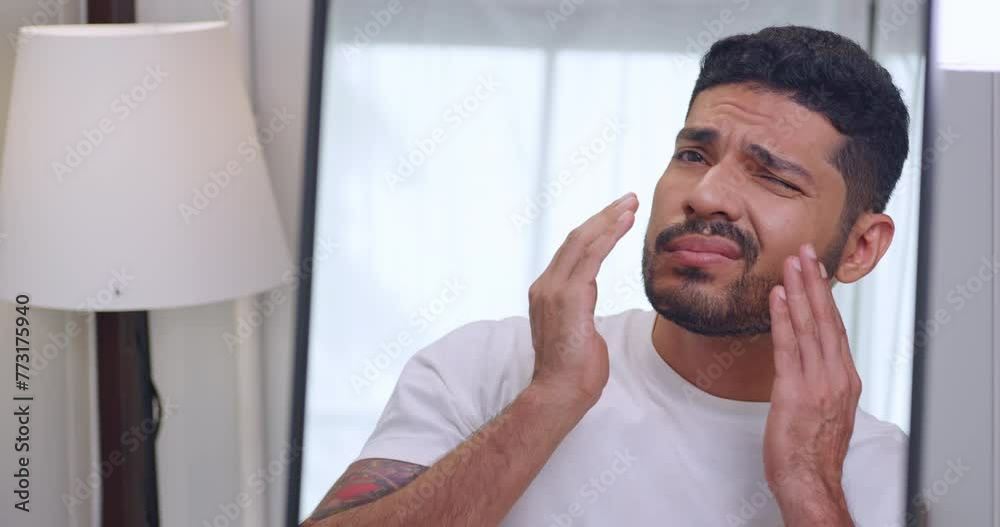 A handsome young man is worried about the wrinkles on his face while looking in the mirror.