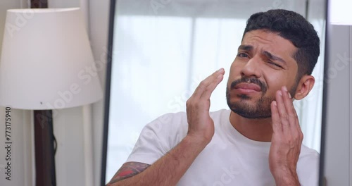 A handsome young man is worried about the wrinkles on his face while looking in the mirror.