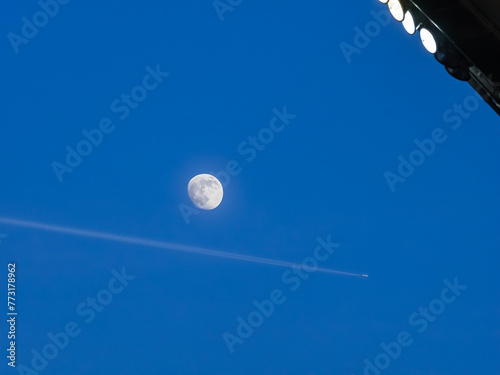 Lune dans le ciel d'un stade de foot avec un avion jet qui laisse une trace dans le ciel bleu en fin de journée photo