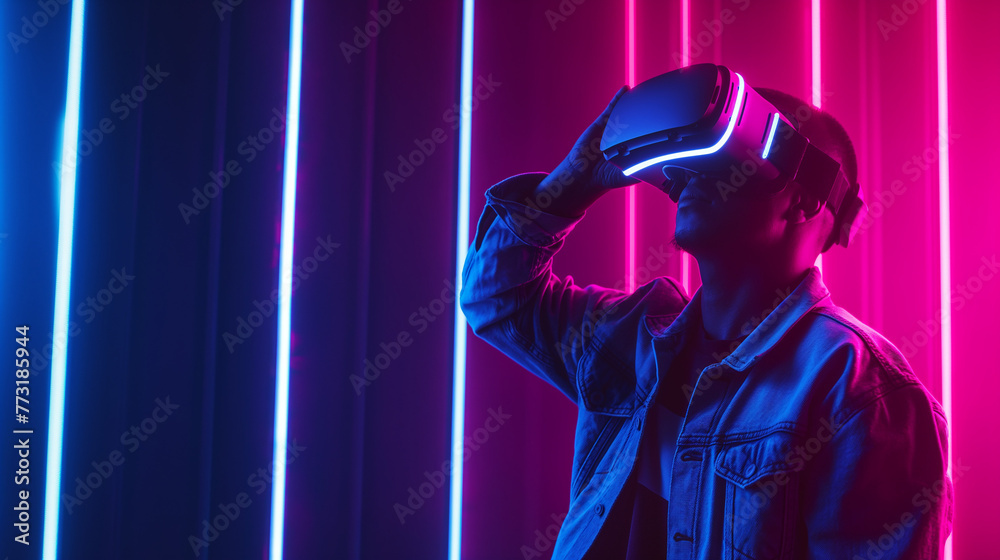 A young excited boy or man is using a virtual reality goggles headset or VR box in a neon light dark background. Futuristic 3D cyber space, modern digital technology, Augmented reality concept.