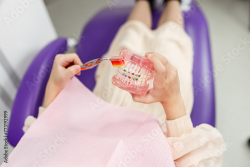 Little girl holding an artificial human jaw model with dental braces in an orthodontic office, smiling. Pediatric dentistry, aesthetic dentistry, early education and prevention.