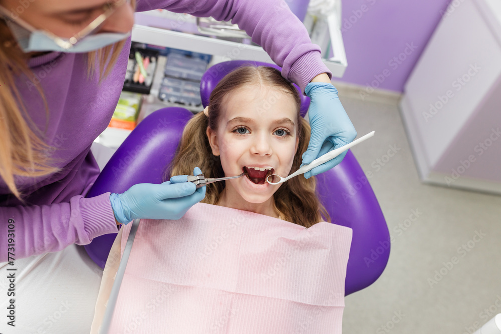 Portrait of a cute little girl laughing looking at camera sitting in stomatology seat while pediatric stomatologist is ready to do teeth examination Portrait of a cute little girl laughing looking at camera sitting in stomatology seat while pediatric stomatologist is ready to do teeth examination