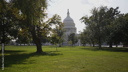 View of US Capitol through trees and green grass in Washington, DC on a sunny summer fall day.