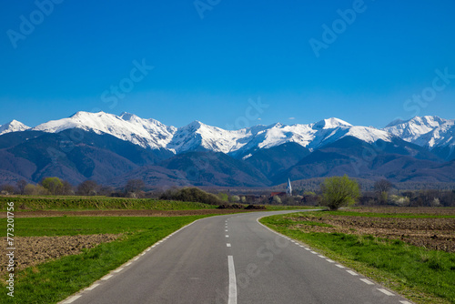 Landscape with a road leading to a village and in the background the Fagaras mountains with their peaks covered with snow. Perfect for wallpaper or design. Beautiful landscape from Romania