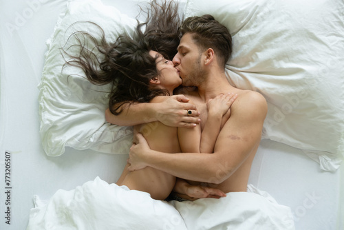 Top view Portrait of romantic, attractive, contented, young, hugging, kissing sexy loving couple nude in white bed