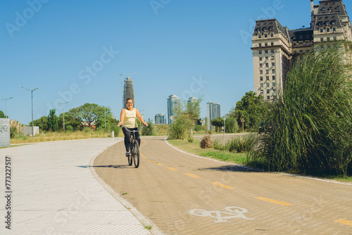 happy middle-aged latin woman riding a bike in the city, doing physical activity. copy space